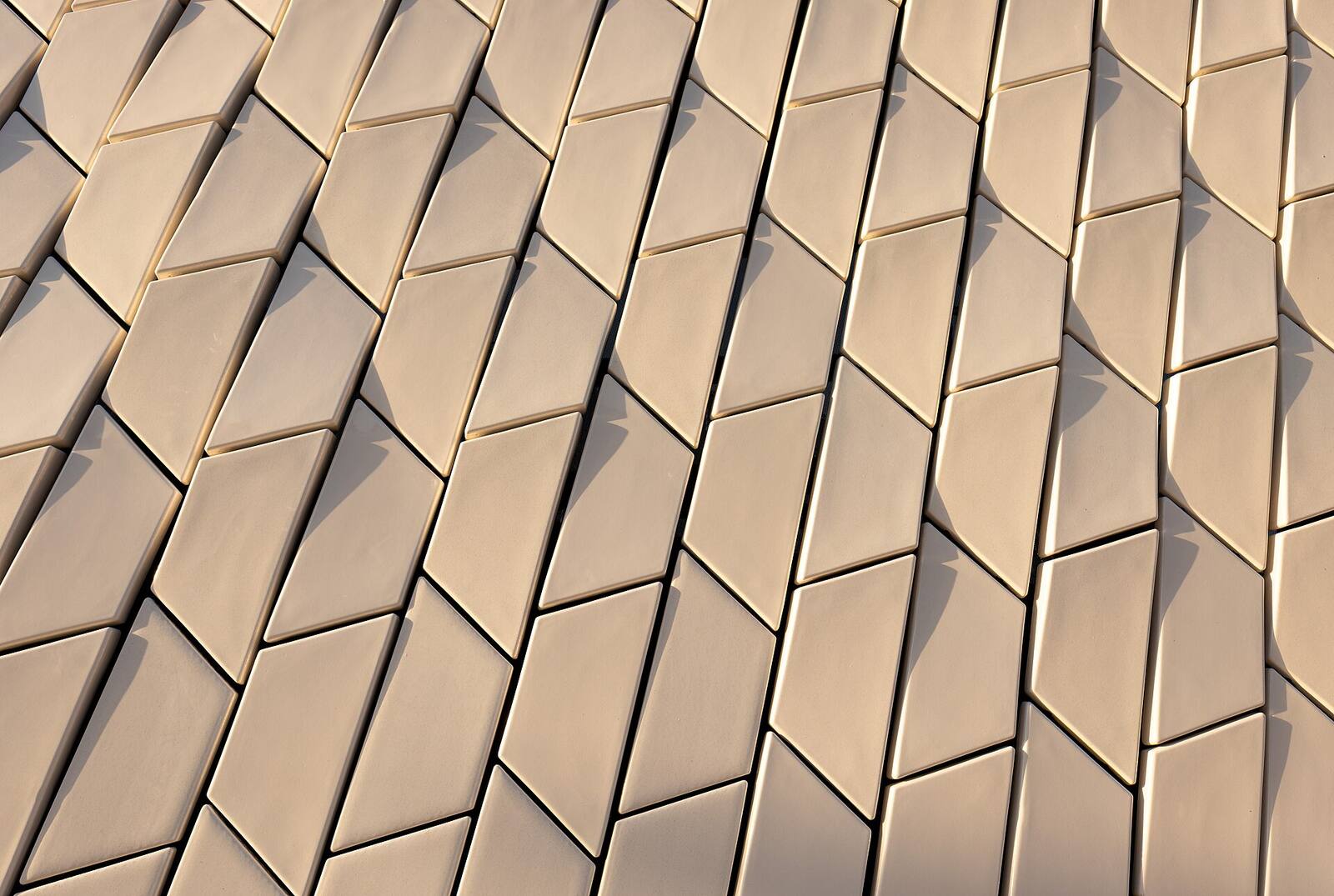 Close-up of overlapping diamond-shaped ceramic facade tiles in soft light