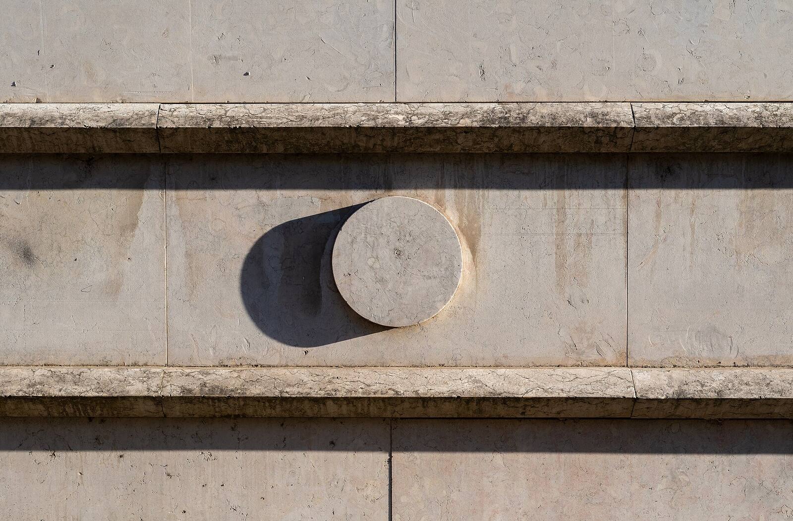 Close-up of a pale stone facade with a carved round boss between horizontal bands
