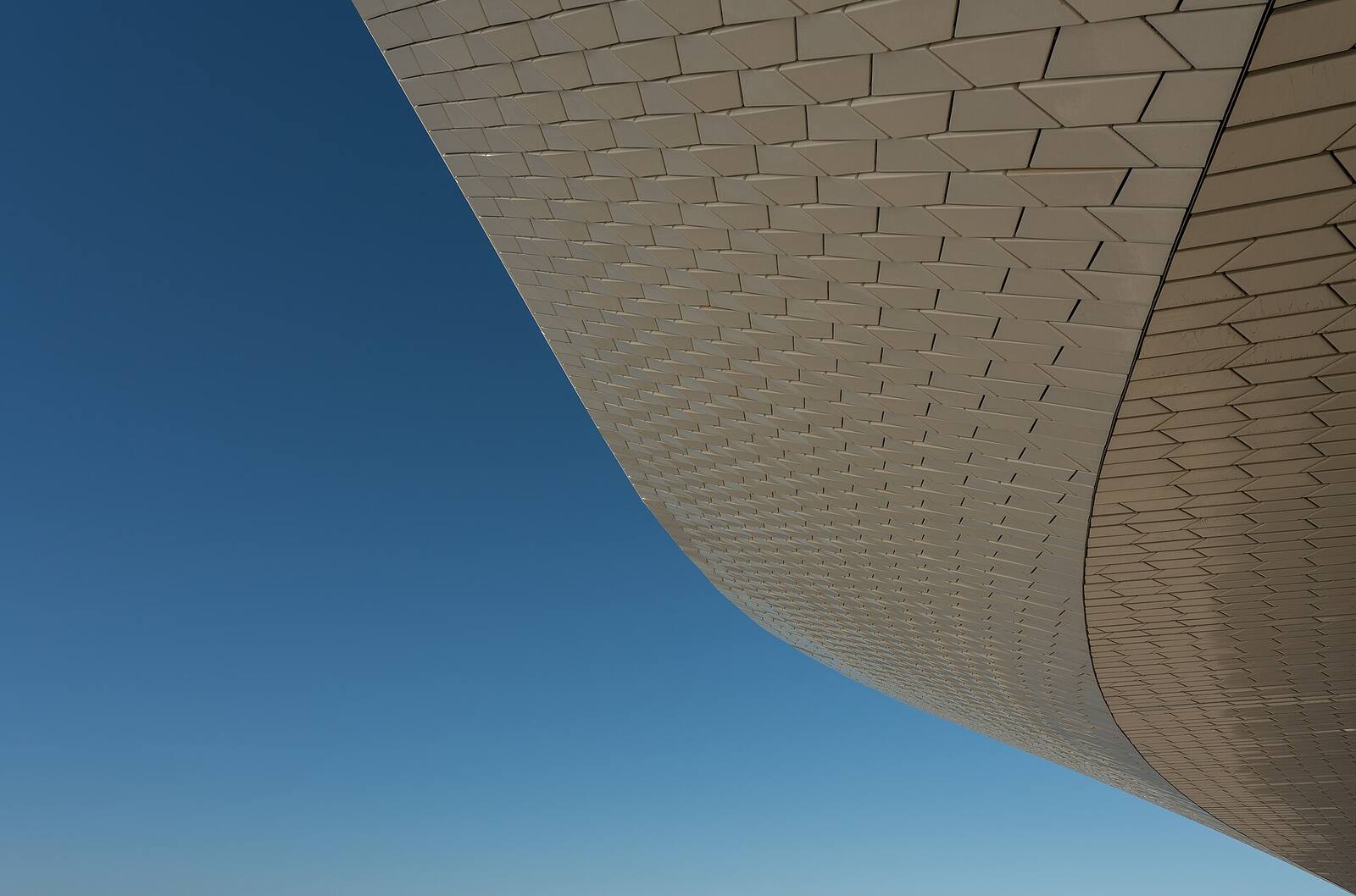 Curved white ceramic-tile facade sweeping against a clear blue sky